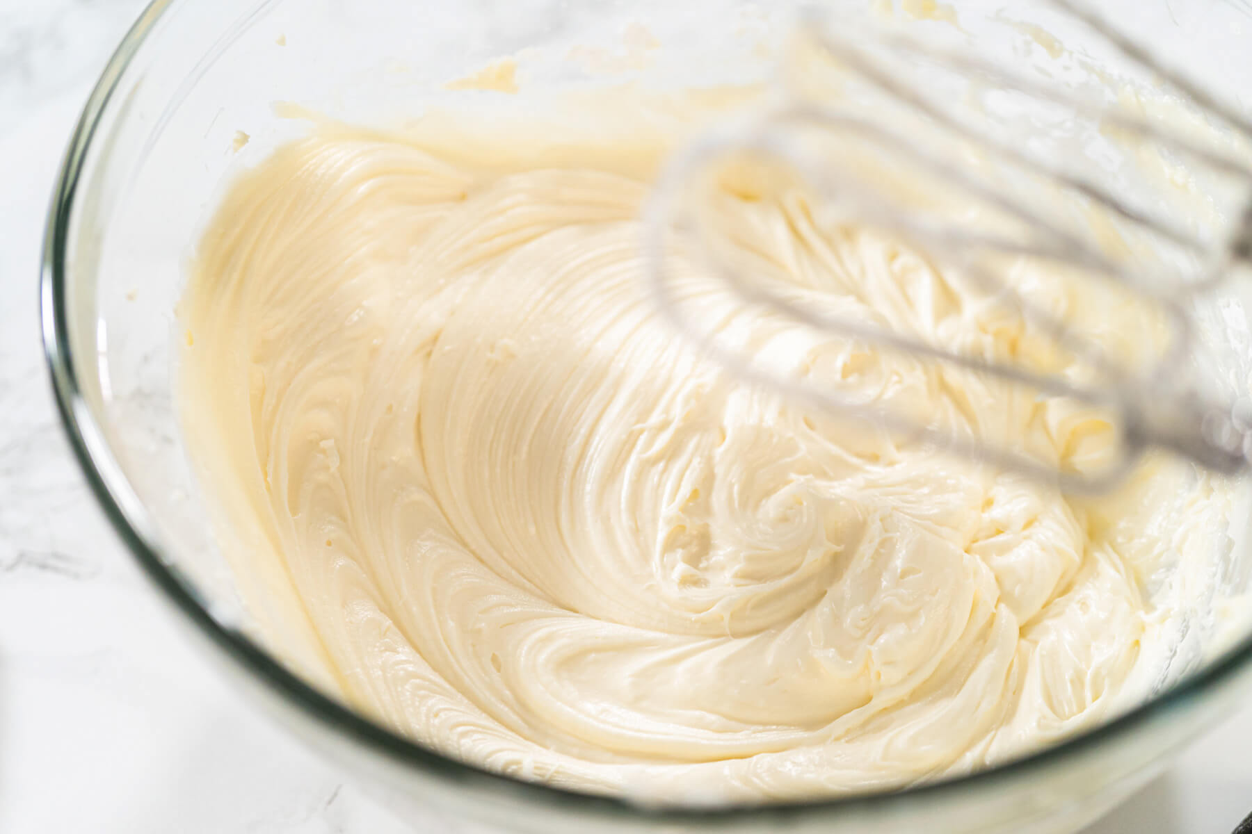 Aufgeschlagene Butter-Zucker-Masse in einer Glasschüssel, noch mit sichtbaren gelblichen Butterstreifen