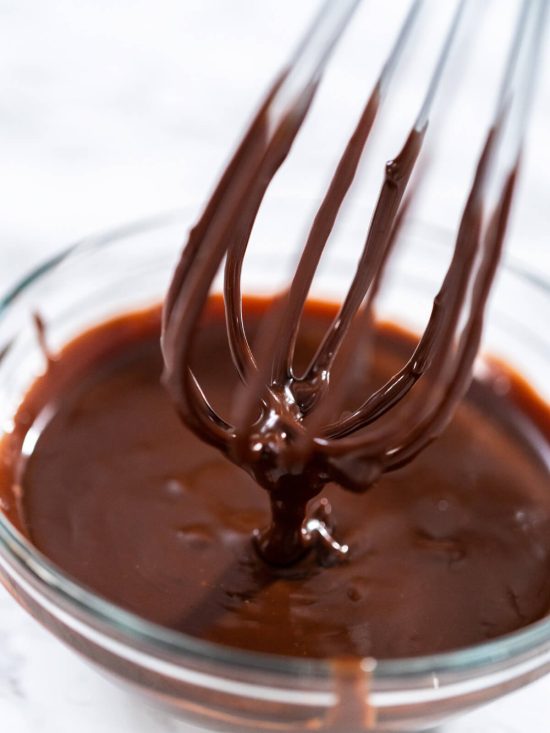 Glänzende dunkle Ganache in einer weißen Schüssel, ein Löffel zieht eine Spur durch die glatte Oberfläche
