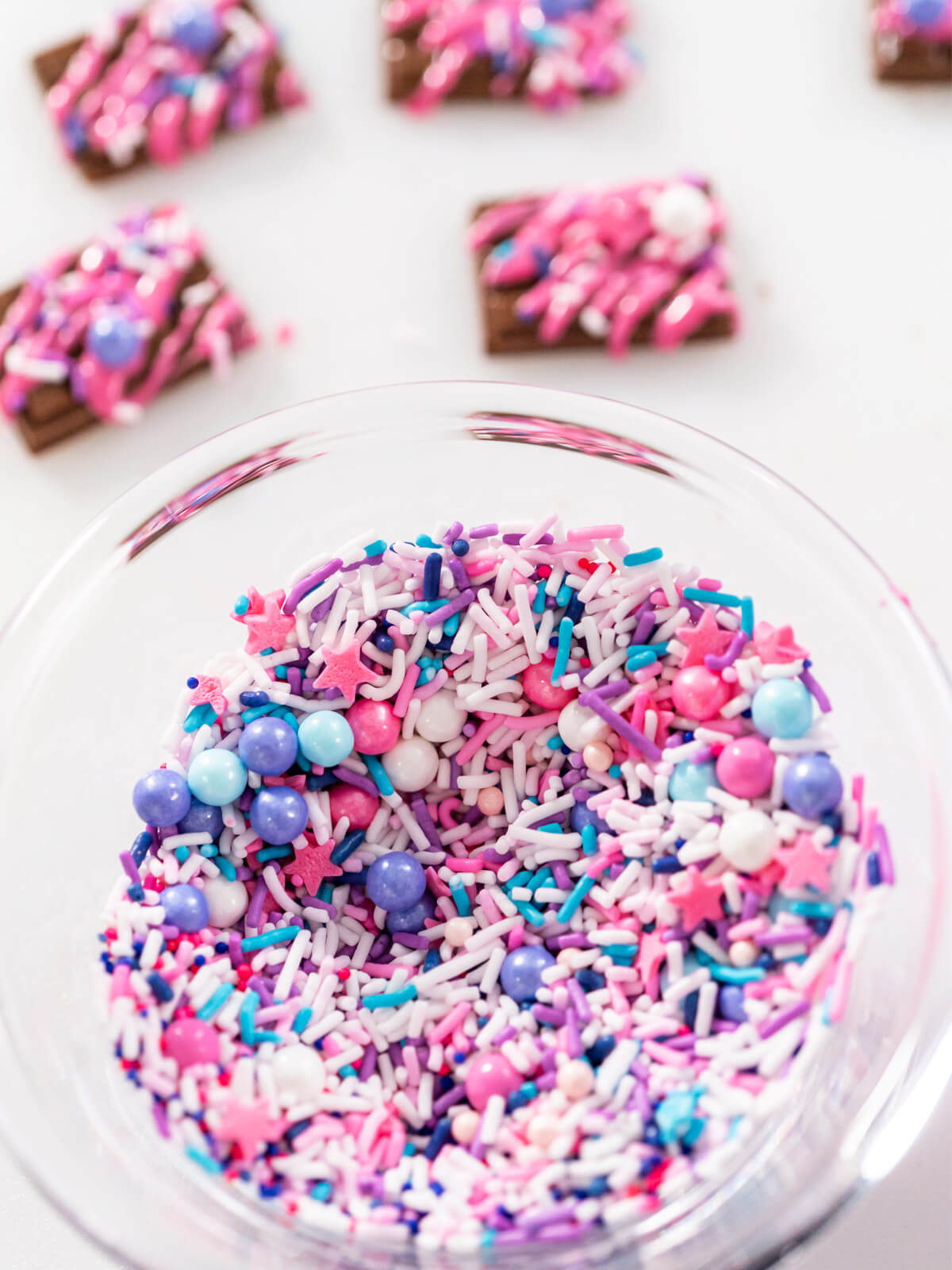 Glasschale mit buntem Streuselmix aus Stäbchen, Zuckerperlen und Sternen in Weiß, Rosa, Violett und Türkis