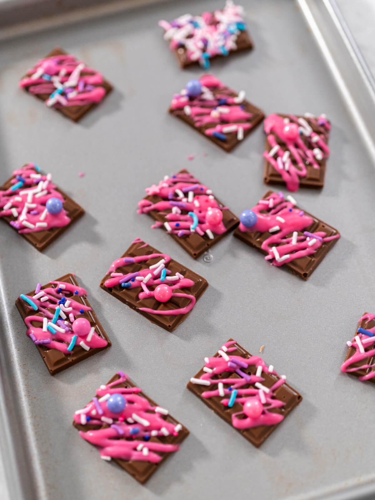 Fertig verzierte Schoko-Topper mit rosa Linien, Zuckerperlen und Streuseln nebeneinander auf einem Backblech