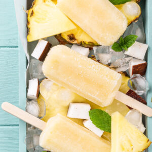 Goldgelbes Ananas-Kokos-Stieleis am Holzstiel mit frischer Ananas und Heidelbeeren