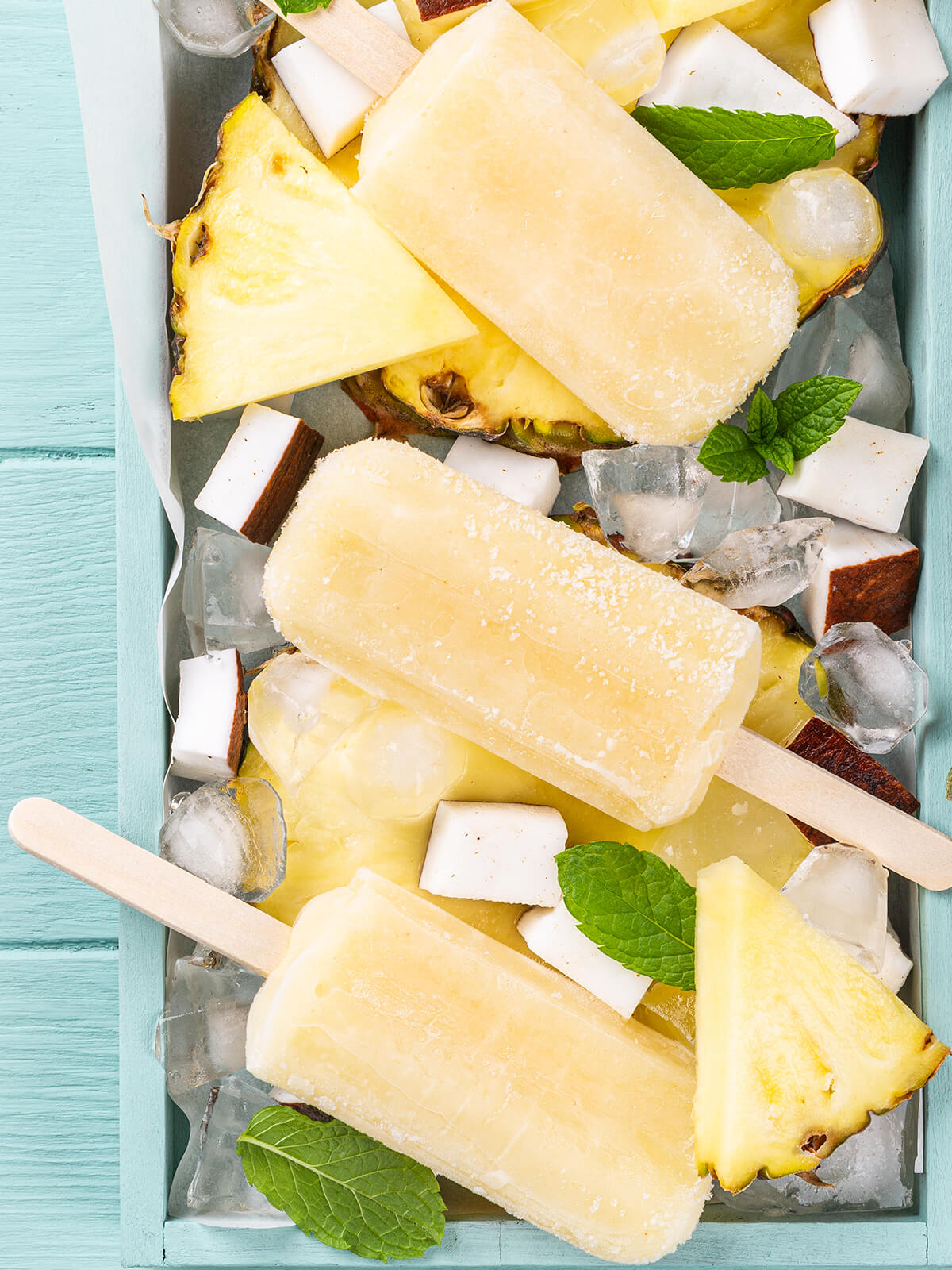 Goldgelbes Ananas-Kokos-Stieleis am Holzstiel mit frischer Ananas und Heidelbeeren