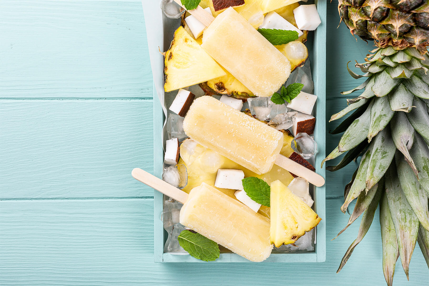 Cremiges Ananas-Kokos-Stieleis am Holzstiel mit Ananasscheiben und Kokosraspeln dekoriert