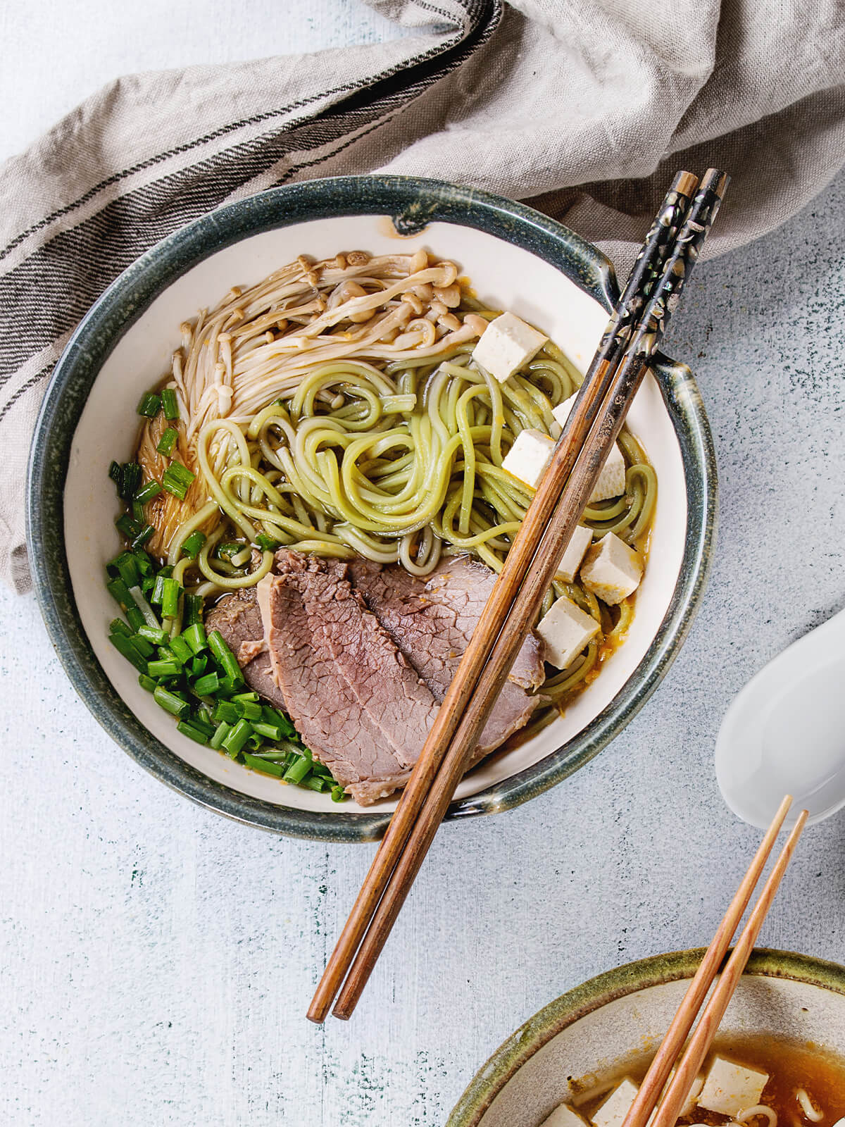 Zwei Schalen asiatische Nudelsuppe mit grรผnen Spinat-Ramen, Rindfleisch, Tofu und Enoki, mit Holzstรคbchen