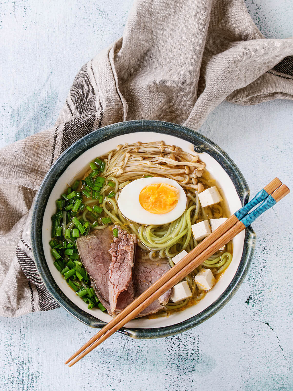 Asiatische Nudelsuppe mit grรผnen Spinat-Ramen, Rindfleisch, Tofu, Enoki und weichem Ei, mit Stรคbchen