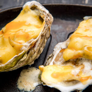 Zwei überbackene Austern mit geschmolzenem Käse und Sahnesauce in gusseiserner Pfanne