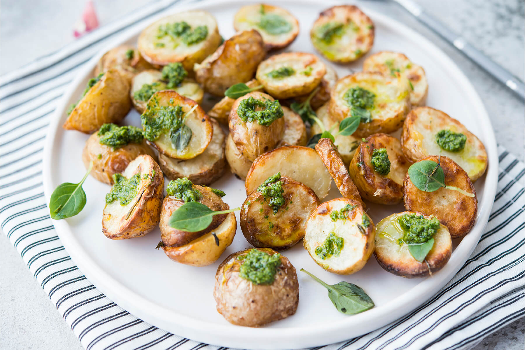 Geröstete Babykartoffeln mit Klecksen aus grünem Basilikum-Pesto auf weißem Teller