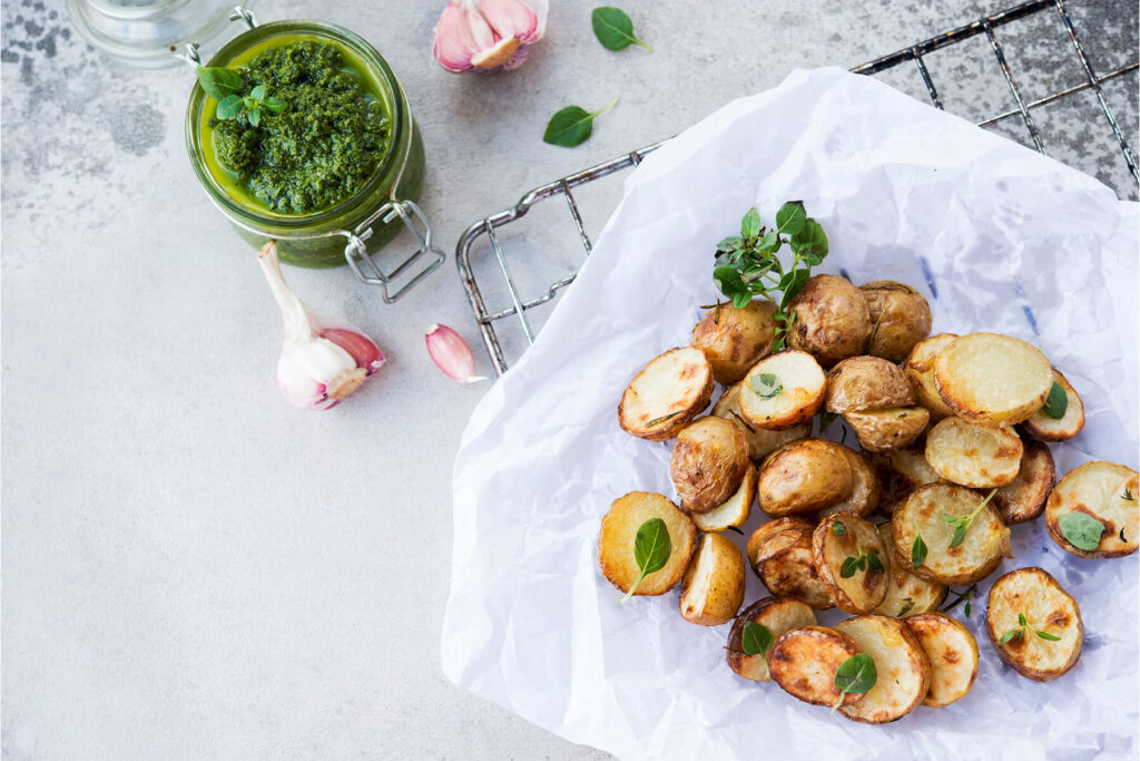Rustikal geröstete halbierte Babykartoffeln mit goldbraunen Schnittflächen und grünem Basilikum-Pesto auf weißem Teller