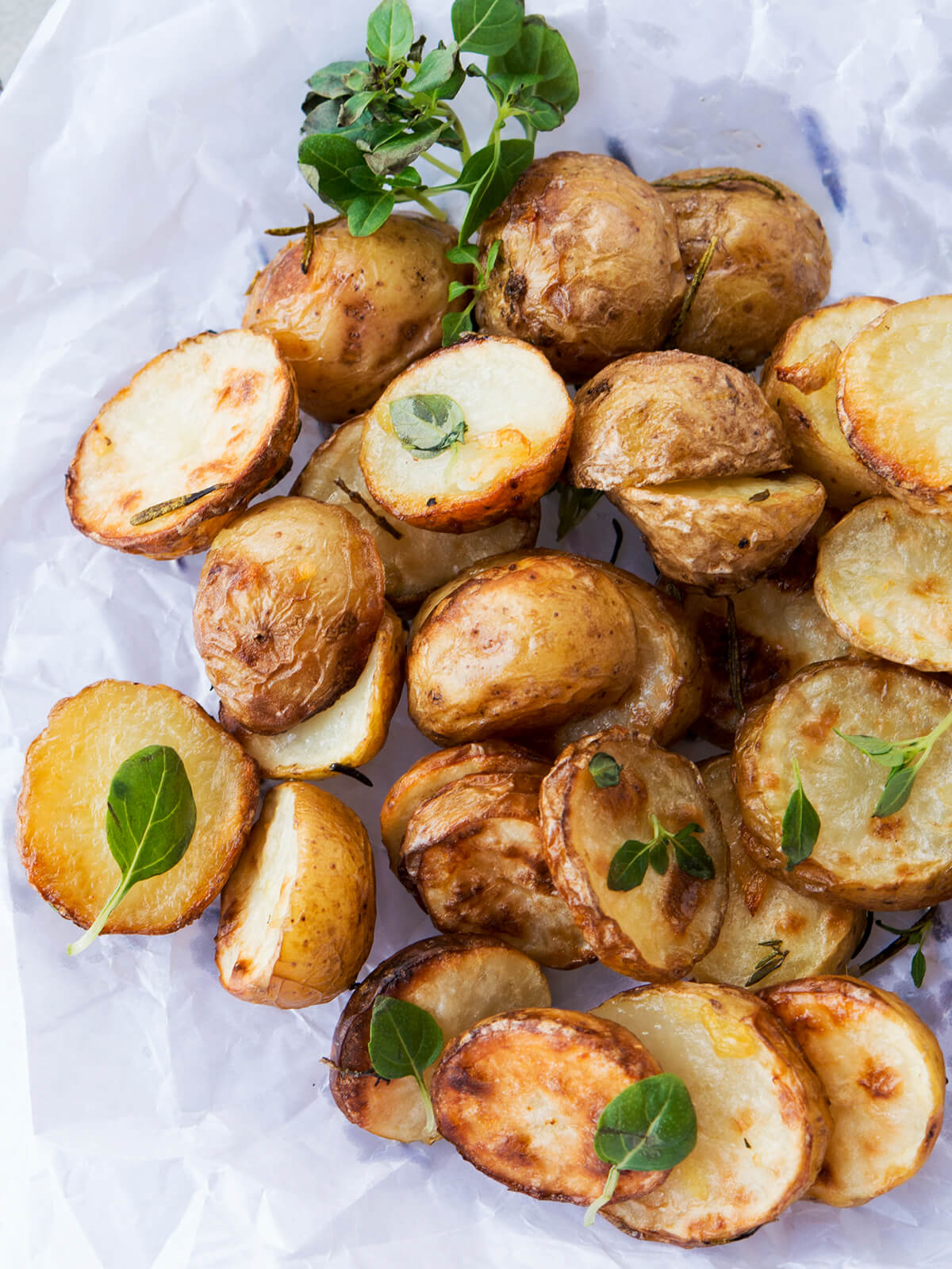 Rustikal geröstete halbierte Babykartoffeln mit goldbraunen Schnittflächen und frischen Kräutern auf Backpapier