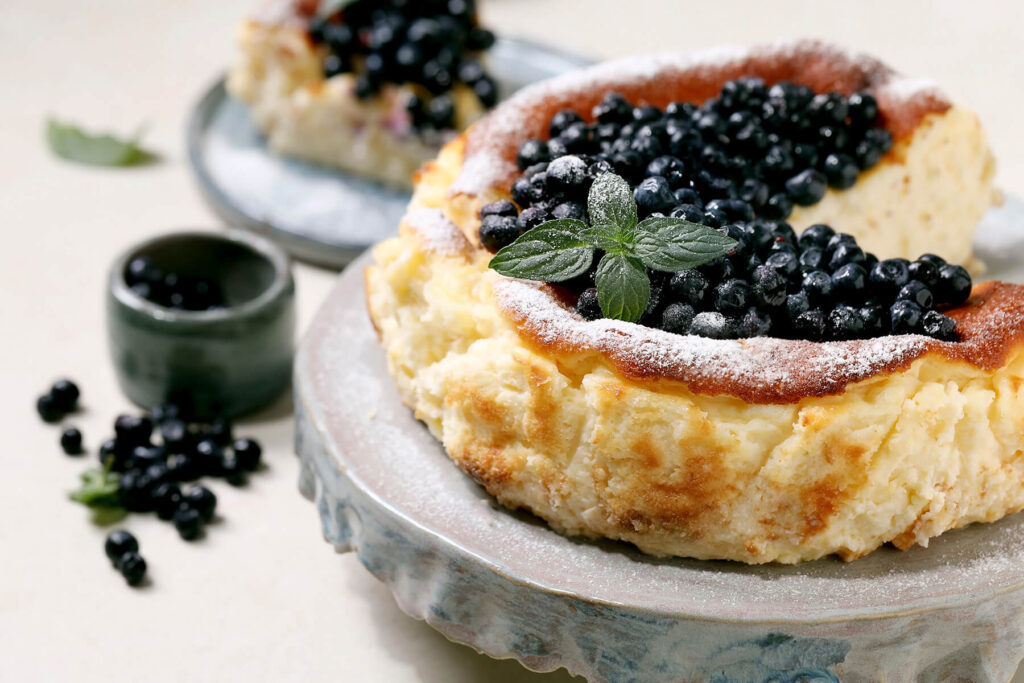 Baskischer Burnt Cheesecake mit Heidelbeeren-Topping, Puderzucker und Minze, dunkel karamellisierte Oberfläche