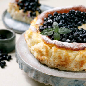 Baskischer Burnt Cheesecake mit Heidelbeeren-Topping, Puderzucker und Minze, dunkel karamellisierte Oberfläche
