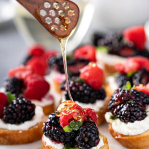 Beeren-Bruschetta mit Ziegenfrischkäse, Brombeeren, Himbeeren, Minze und Honig auf weißer Servierplatte