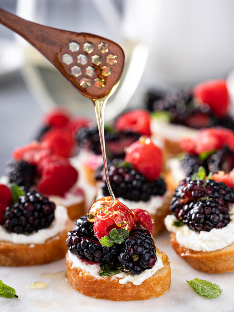 Beeren-Bruschetta mit Ziegenfrischkäse, Brombeeren, Himbeeren, Erdbeeren, Minze und Honig auf weißer Servierplatte