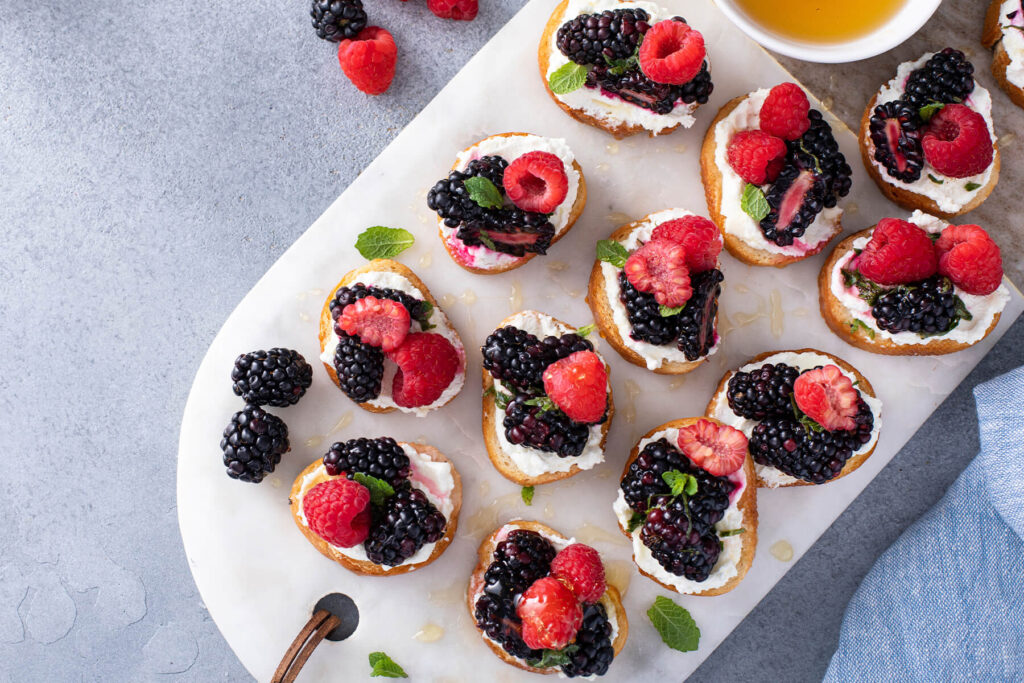 Beeren-Bruschetta mit Ziegenfrischkäse, Brombeeren, Himbeeren, Erdbeeren und Honig auf goldgerösteten Baguettescheiben mit Minze