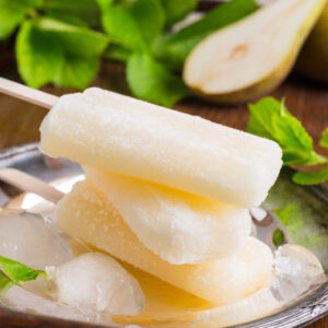 Cremig-weiße Birnen-Sorbet-Stieleis-Stücke auf silbernem Tablett mit Crushed Ice und halber frischer Birne