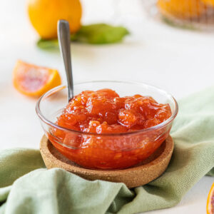 Hausgemachte Blutorangen-Marmelade in einer Glasschale auf grüner Leinenserviette mit halbierten Blutorangen