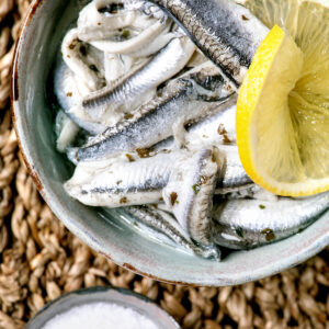 Spanische Boquerones en Vinagre – milchig-weiße Sardellen-Filets mit Zitrone, Olivenöl und Salz auf Holzbrett