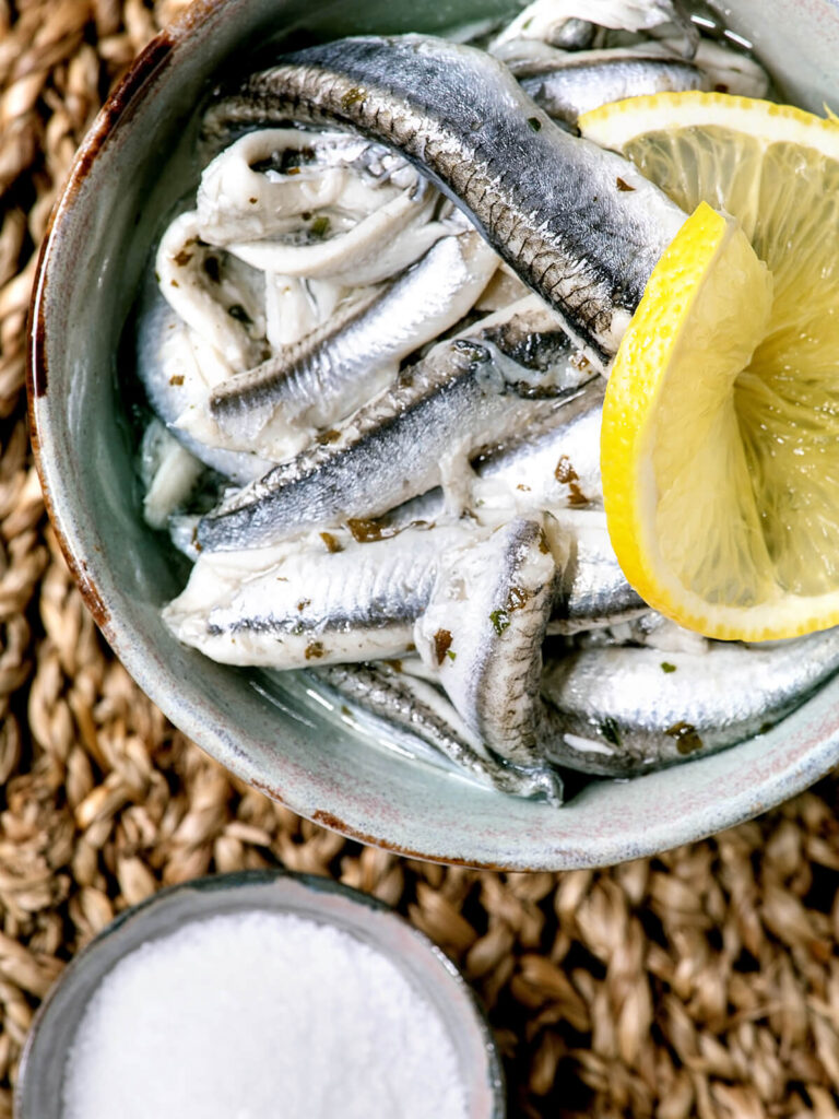 Spanische Boquerones en Vinagre – milchig-weiße Sardellen-Filets mit Zitrone, Olivenöl und Salz auf Holzbrett