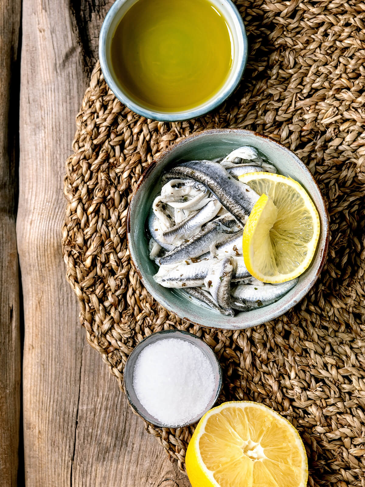 Spanische Boquerones en Vinagre – weiße marinierte Sardellen-Filets mit Zitronenscheibe in Keramikschale auf Strohmatte