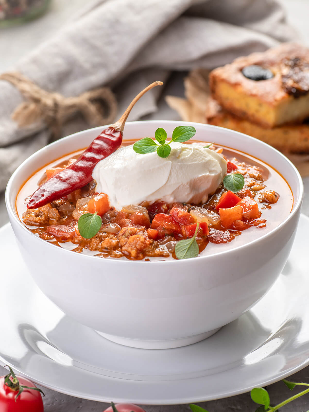 Chili con Carne in hoher weißer Schale mit Schmand, Oregano und einer getrockneten Chilischote