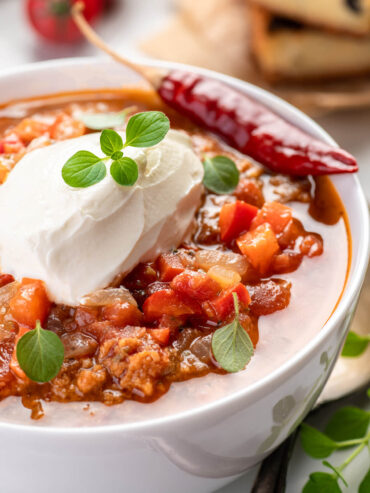 Chili con Carne mit Schmand, frischem Oregano und einer getrockneten Chilischote, Nahaufnahme
