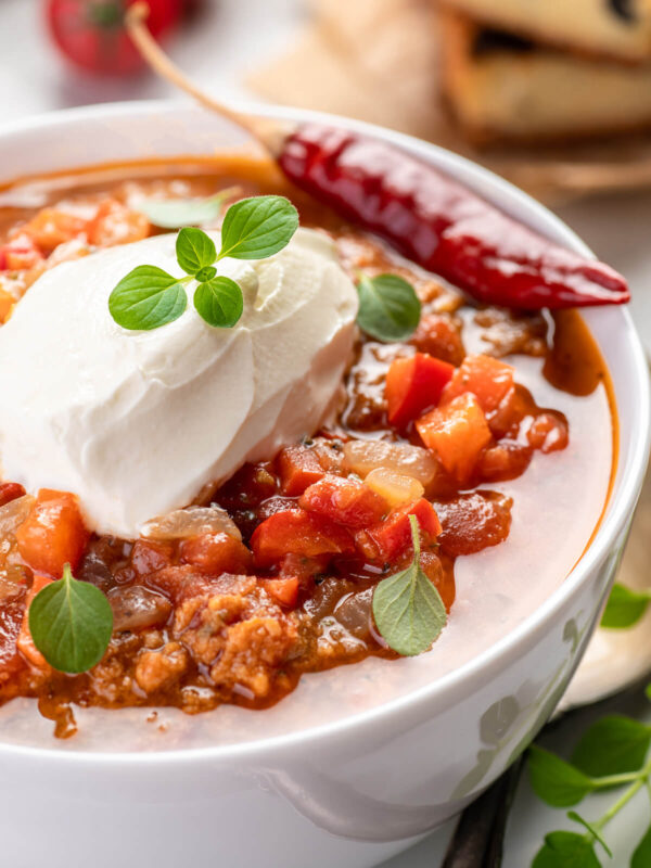 Chili con Carne mit Schmand, frischem Oregano und einer getrockneten Chilischote, Nahaufnahme