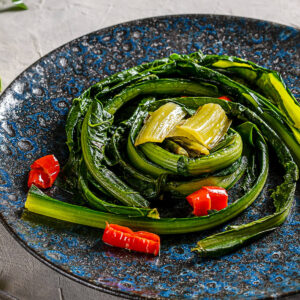 Römische Zikorie mit Knoblauch und Chili auf dunklem Keramikteller als Contorno serviert