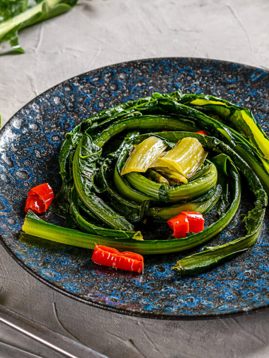 Römische Zikorie mit Knoblauch und Chili auf dunklem Keramikteller als Contorno serviert