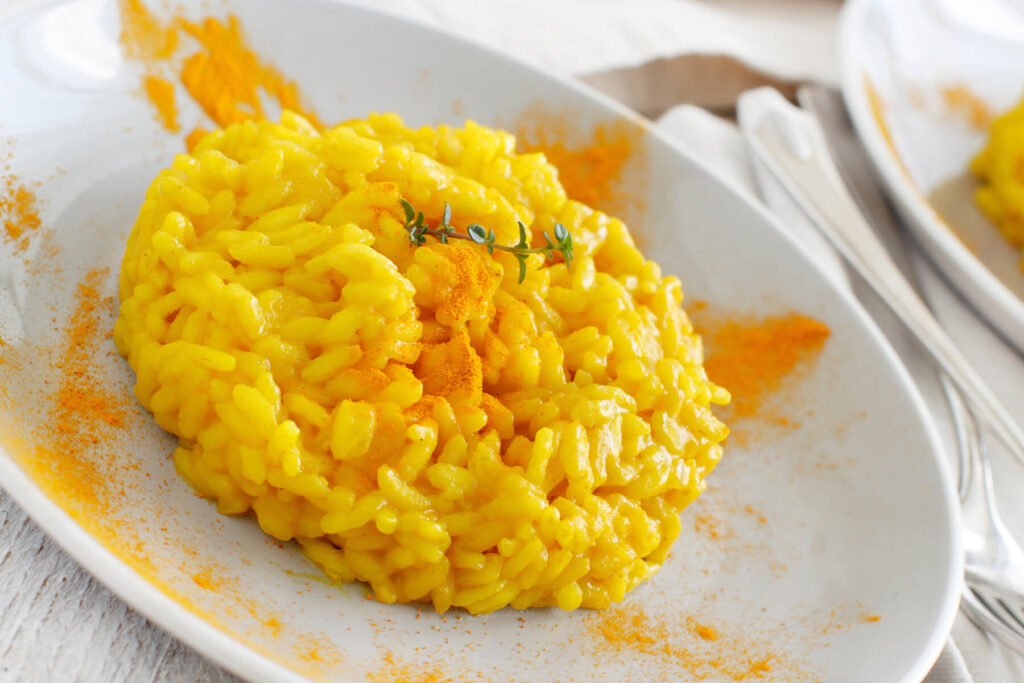 Cremiges Kurkuma-Risotto auf weißem Teller mit goldgelber Farbe und feinem Kurkumapulver-Sprenkel