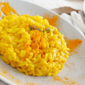 Cremiges Kurkuma-Risotto auf weißem Teller mit goldgelber Farbe und feinem Kurkumapulver-Sprenkel