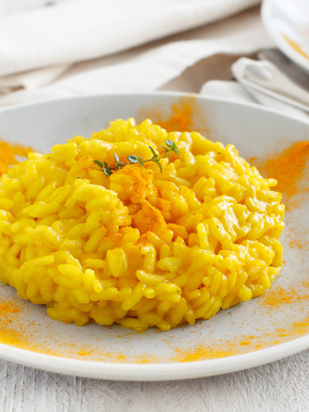 Leuchtend gelbes Kurkuma-Risotto auf weißem Teller mit frischem Thymian und Kurkumapulver-Sprenkel als italienisches Hauptgericht