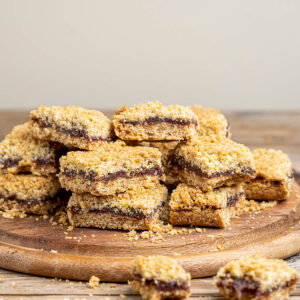 Kanadische Date Squares mit Dattelfüllung zwischen Haferstreuseln auf Holzbrett, daneben Dattelteller und Haferglas