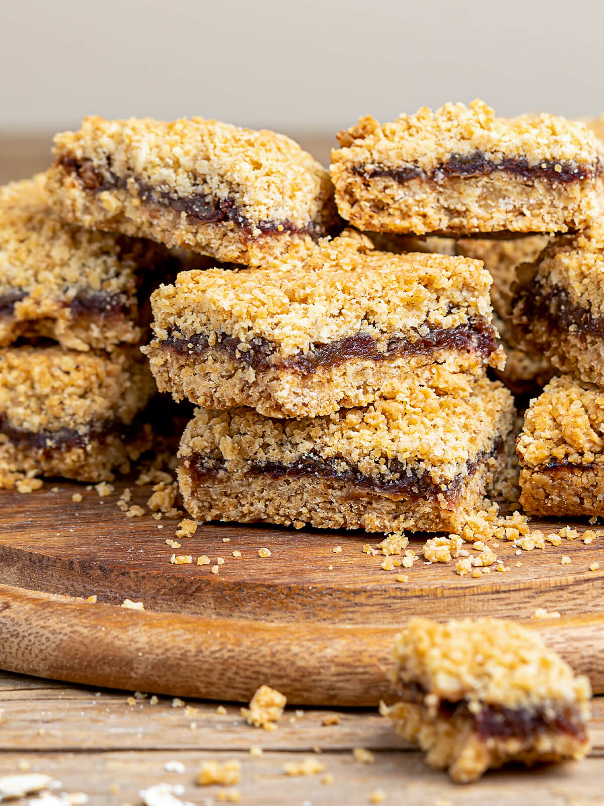 Gestapelte Date Squares mit sichtbarer Dattelfüllung zwischen zwei Haferstreusel-Schichten auf einem Holzbrett