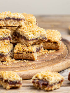 Kanadische Date Squares mit dichter Dattelfüllung zwischen zwei Schichten goldbrauner Haferstreusel auf rustikalem Holzbrett