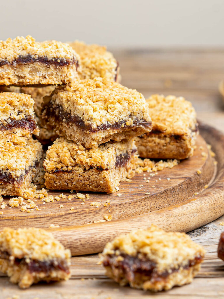 Kanadische Date Squares mit dichter Dattelfüllung zwischen zwei Schichten goldbrauner Haferstreusel auf rustikalem Holzbrett