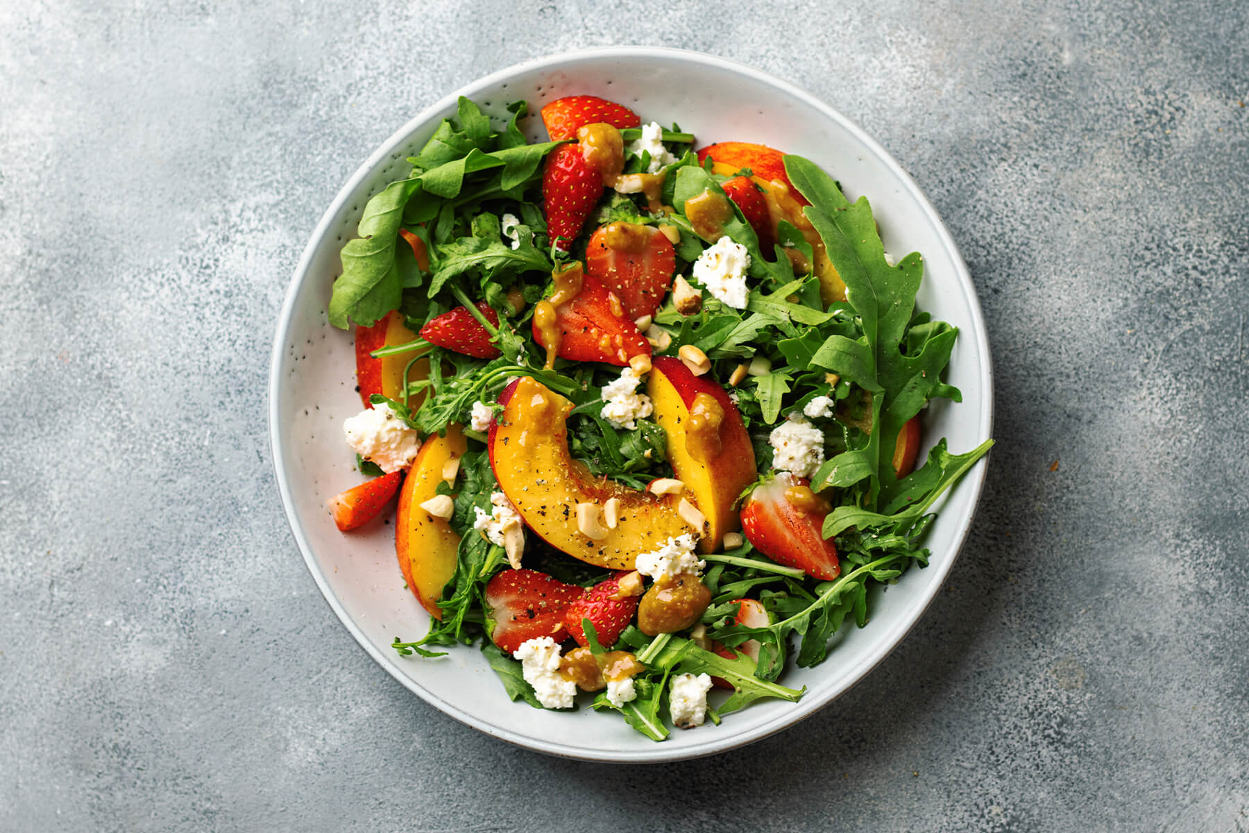 Nahaufnahme des Erdbeer-Nektarine-Salats mit körnigem Hüttenkäse, Rucola und Erdnüssen von oben