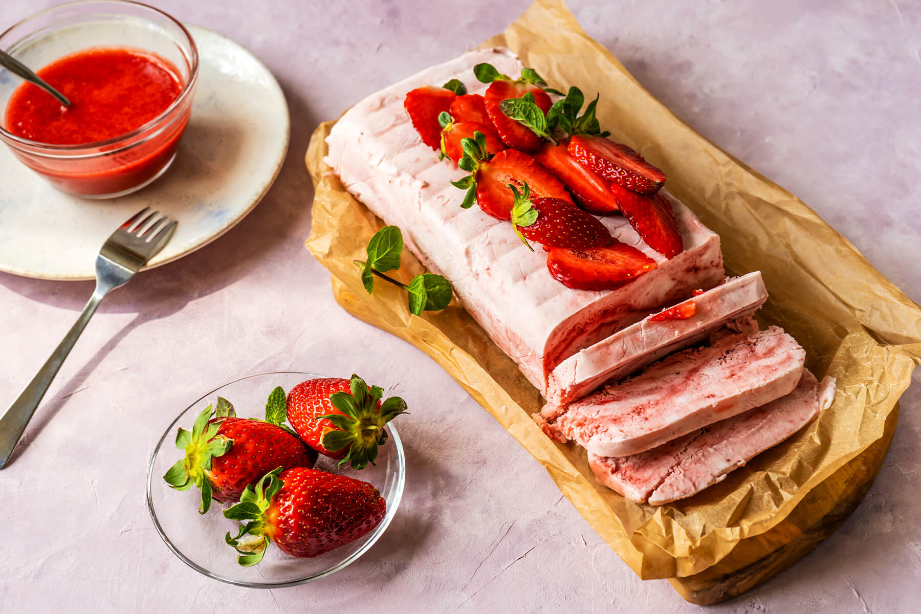 Ganzes Erdbeer-Semifreddo aus der Kastenform, angeschnitten, mit Erdbeeren und einer Schale Coulis