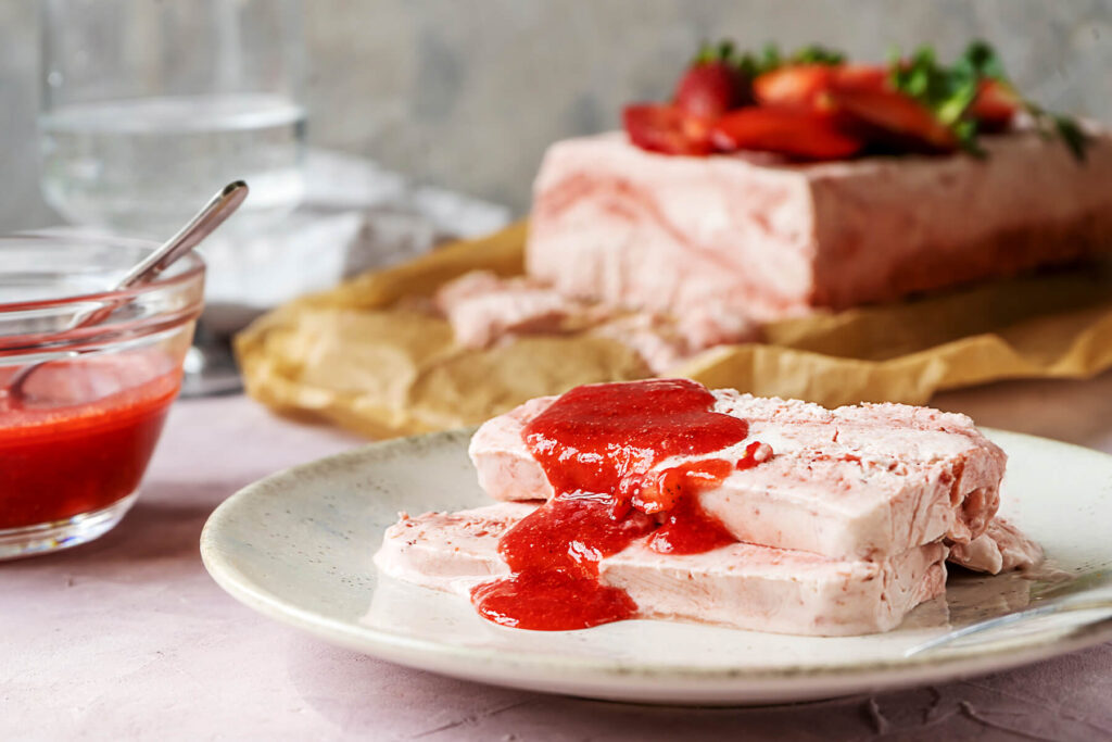 Scheibe Erdbeer-Semifreddo mit frischer roter Erdbeer-Coulis übergossen auf einem Teller