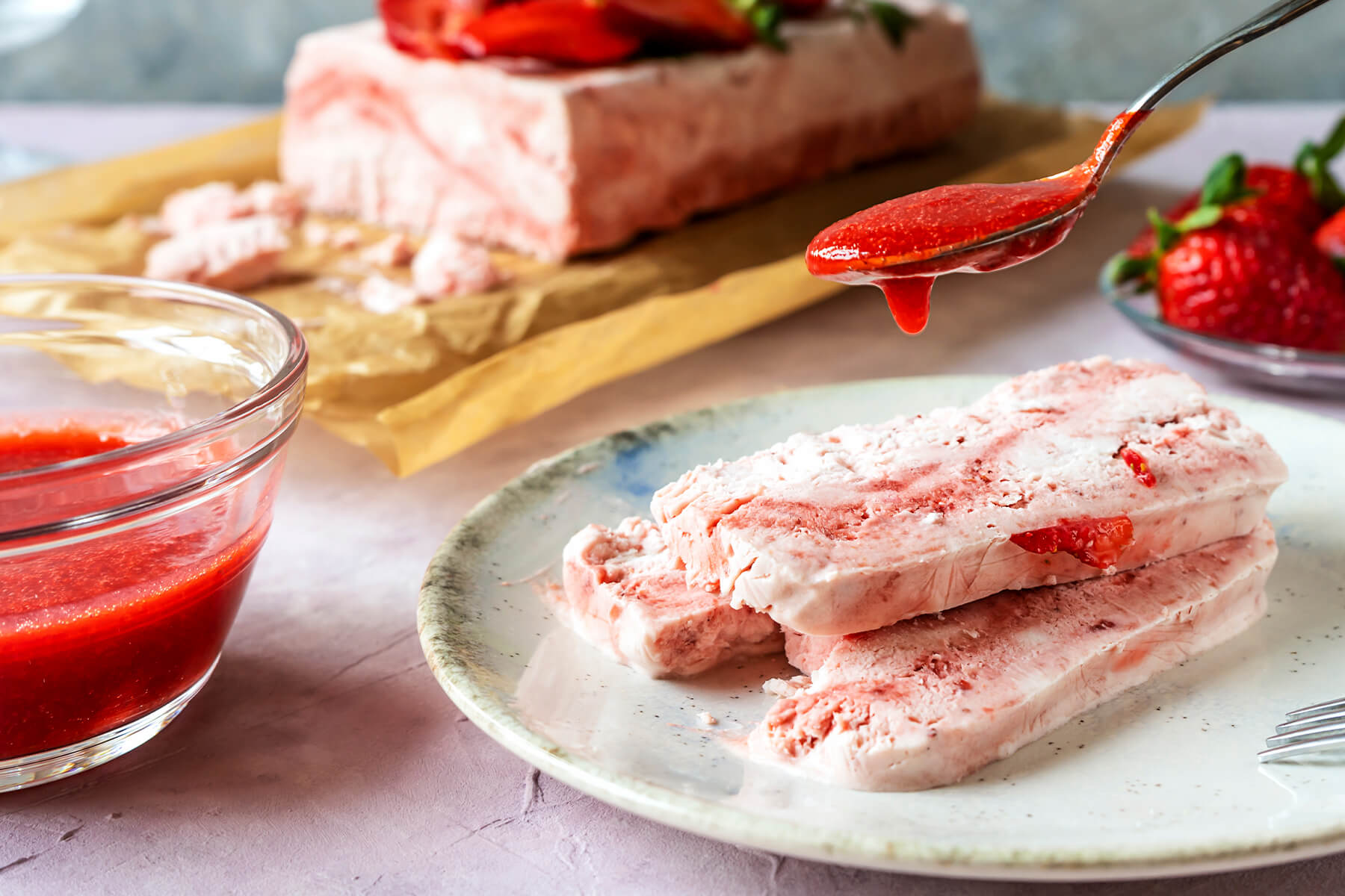 Zwei Scheiben Erdbeer-Semifreddo auf einem Teller, mit Erdbeer-Coulis übergossen