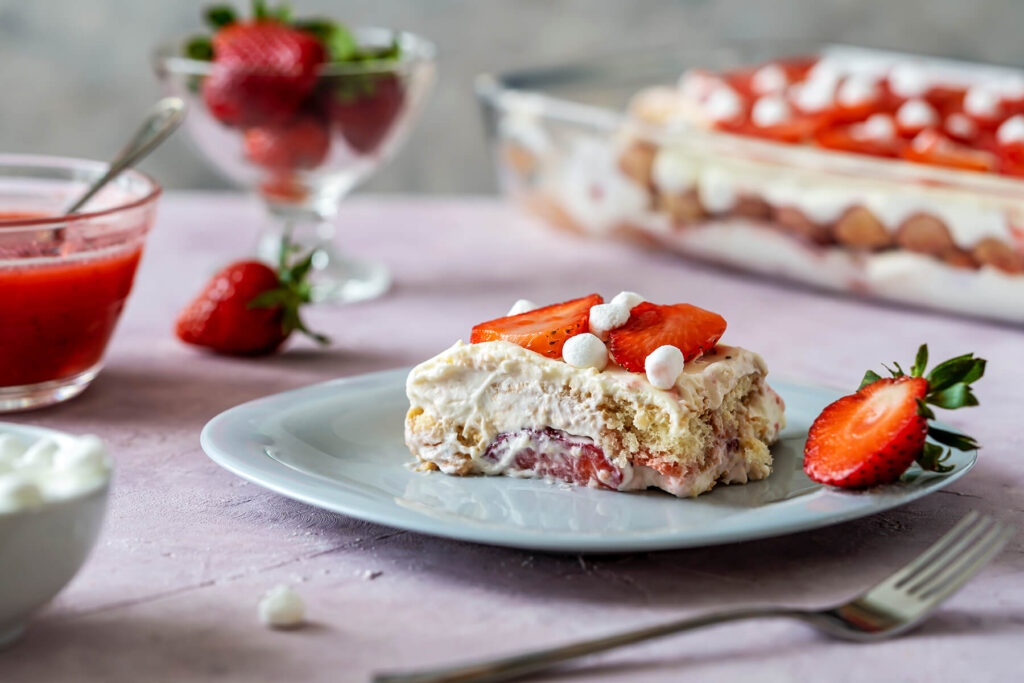 Ein Stück Erdbeer-Tiramisu auf einem Teller mit sichtbaren Creme- und Keksschichten