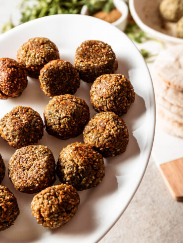 Falafel mit gesprenkelter Sesamhülle auf weißem Teller, dazu Pita und weiße Tahini-Sauce