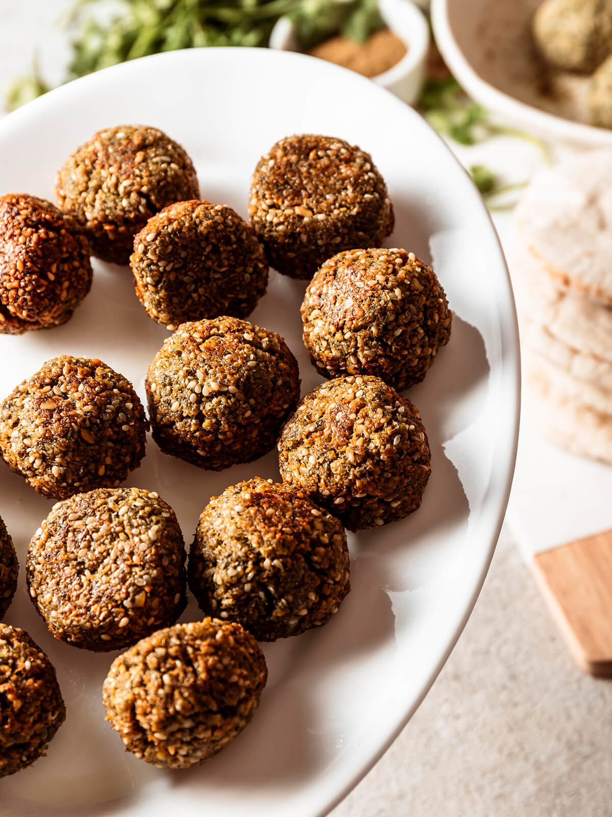 Falafel mit gesprenkelter Sesamhülle auf weißem Teller, dazu Pita und weiße Tahini-Sauce