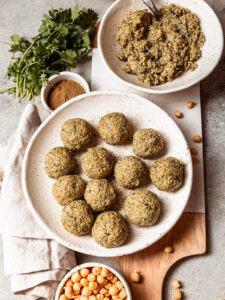 Geformte rohe Falafel-Kugeln und körnige, kräuterdurchsetzte Kichererbsen-Masse vor dem Frittieren