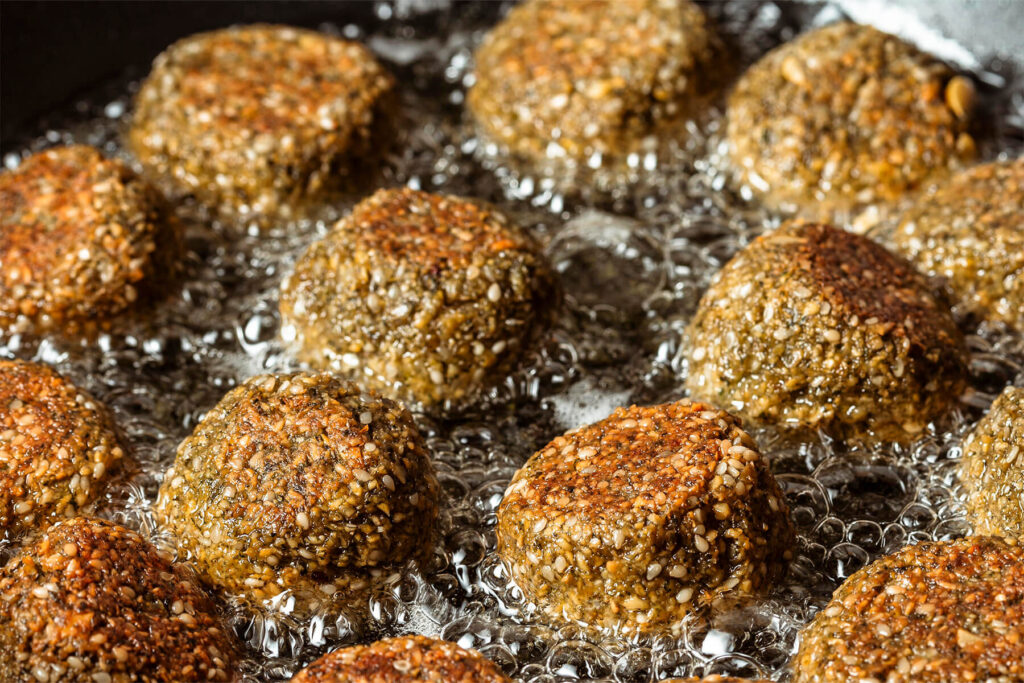 Falafel-Bällchen mit Sesamhülle in flachem heißem Öl, unten goldbraun, oben noch hell