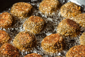 Falafel-Bällchen mit Sesamhülle in flachem heißem Öl, unten goldbraun, oben noch hell