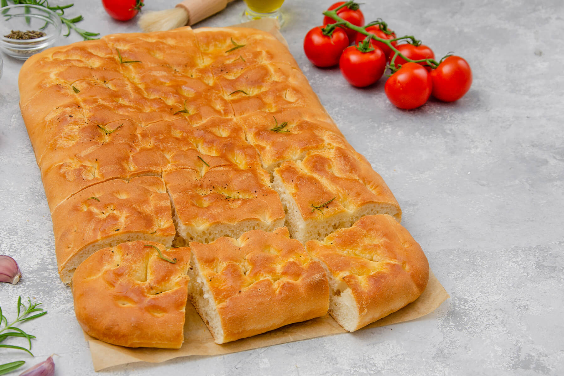 Goldbraune Focaccia mit Rosmarin und schwarzem Pfeffer, in Stücke geschnitten, mit Kirschtomaten und Knoblauch
