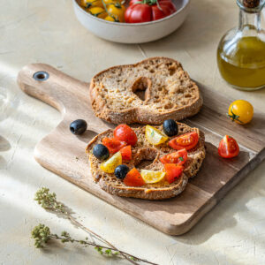 Apulische Frisella mit roten und gelben Kirschtomaten, schwarzen Oliven und Oregano auf hellem Holzbrett