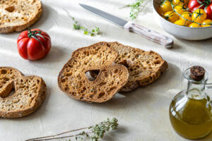 Friselle-Brotringe mit frischen Kirschtomaten, Olivenöl und Kräutern auf heller Arbeitsfläche
