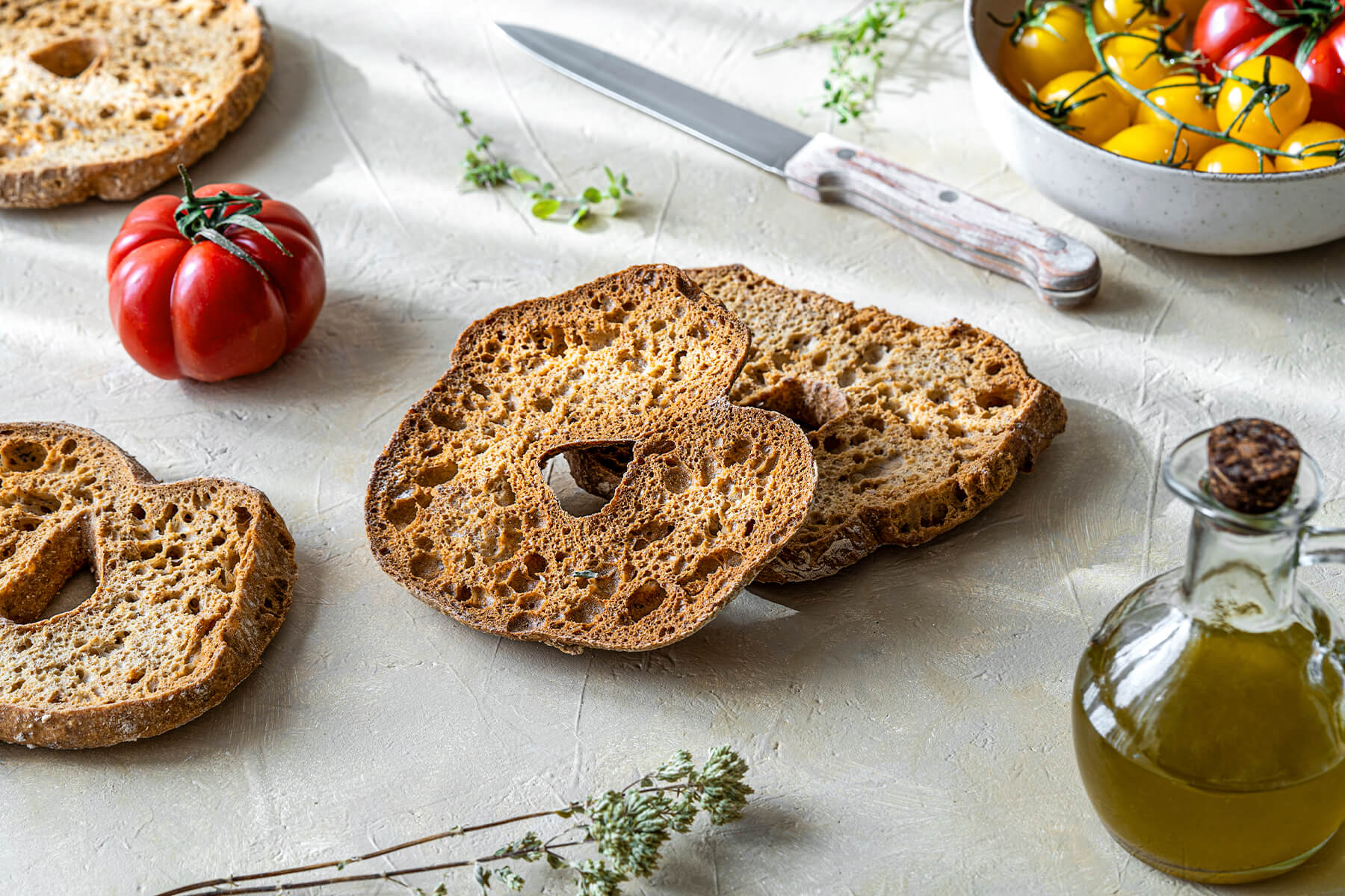 Friselle-Brotringe mit frischen Kirschtomaten, Olivenöl und Kräutern auf heller Arbeitsfläche
