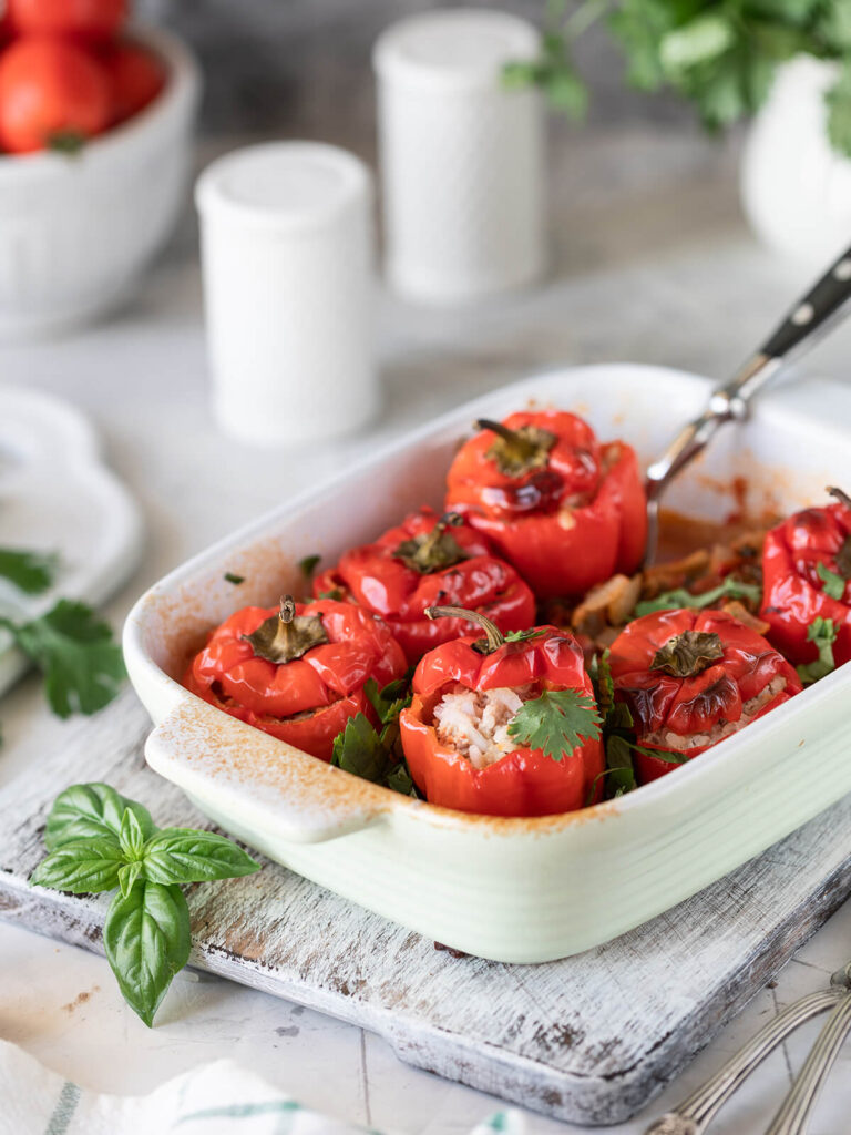 Gefüllte rote Paprika mit grünem Stiel in heller Auflaufform nach dem Schmoren